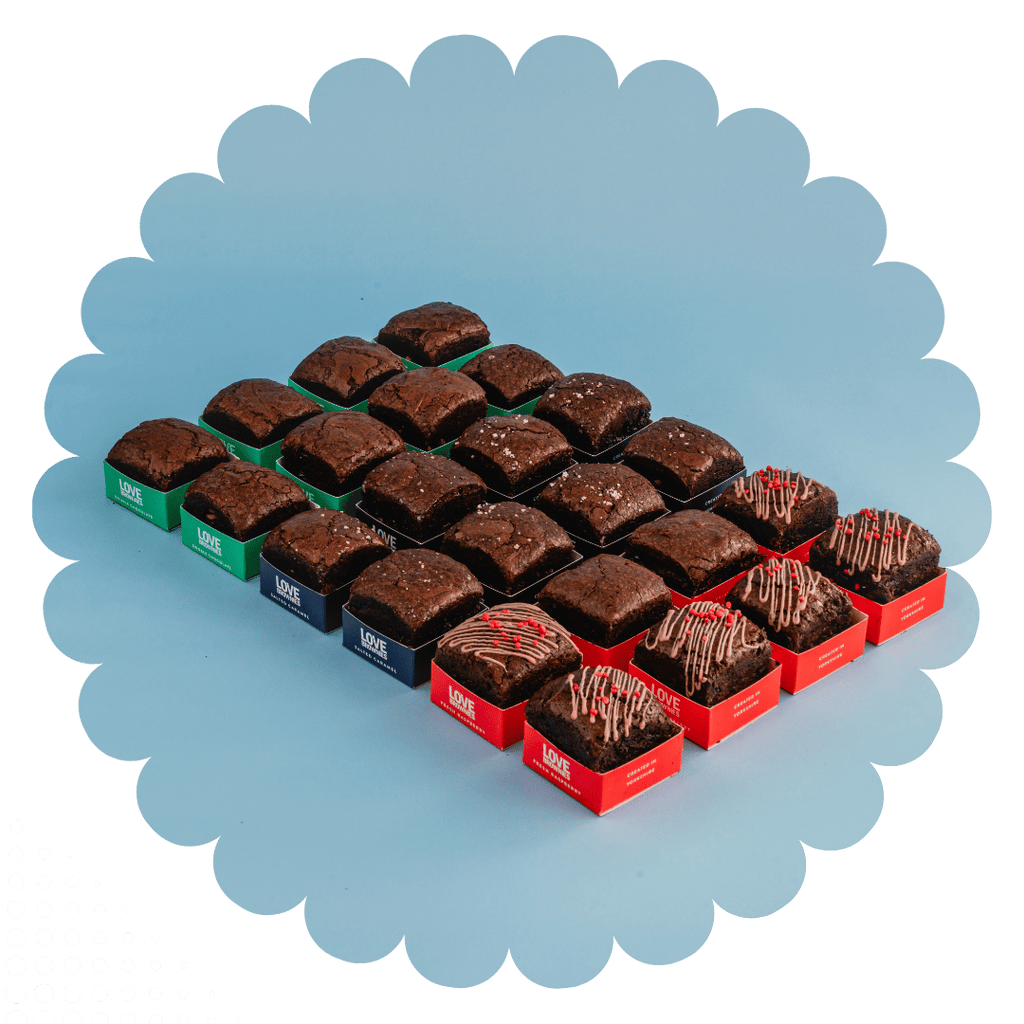 24 gluten-free handmade chocolate brownies in different packaging depending on flavour - red for raspberry, blue for salted caramel, green for double chocolate - on a blue background
