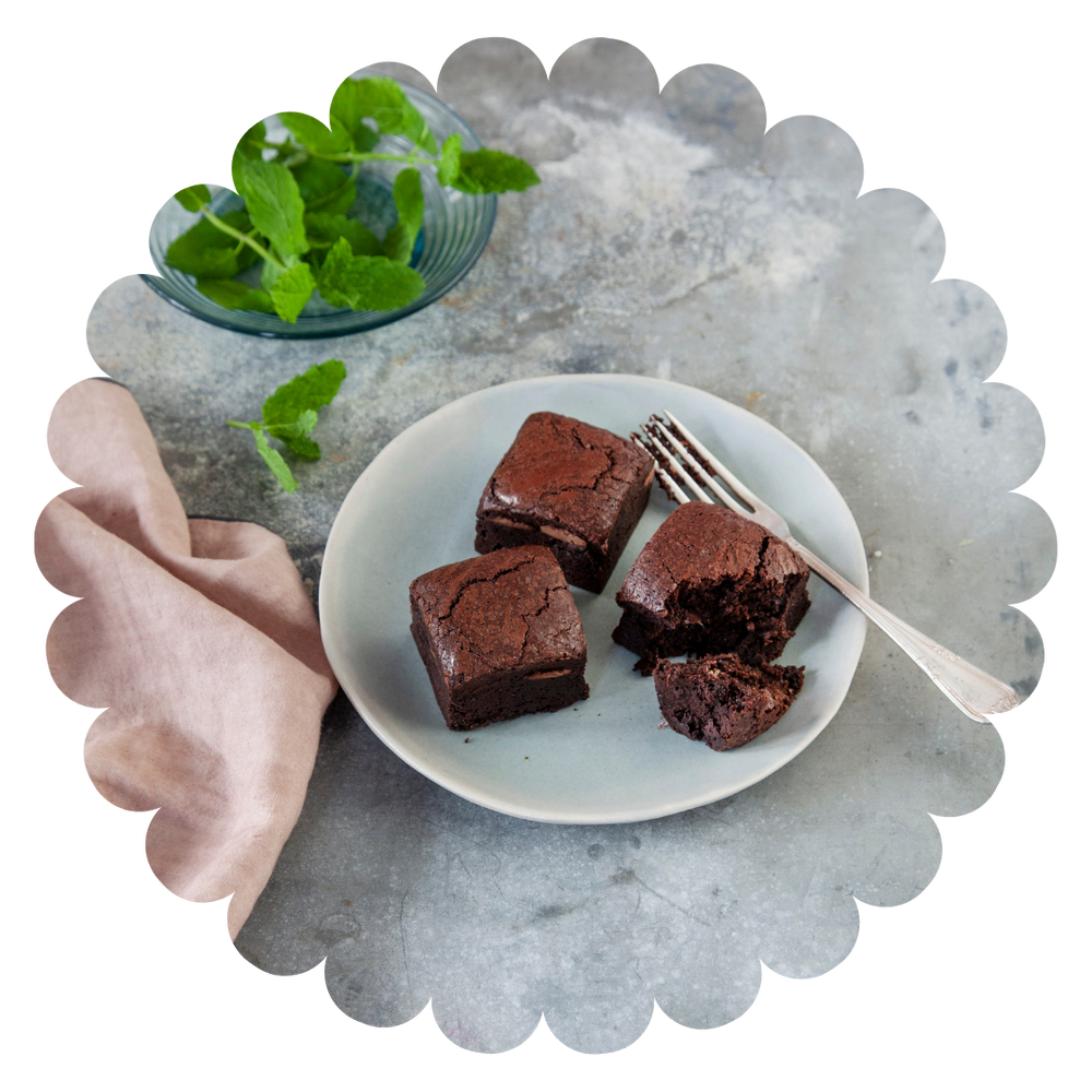 Moist mint flavoured gluten free chocolate brownies on a plate with fresh mint