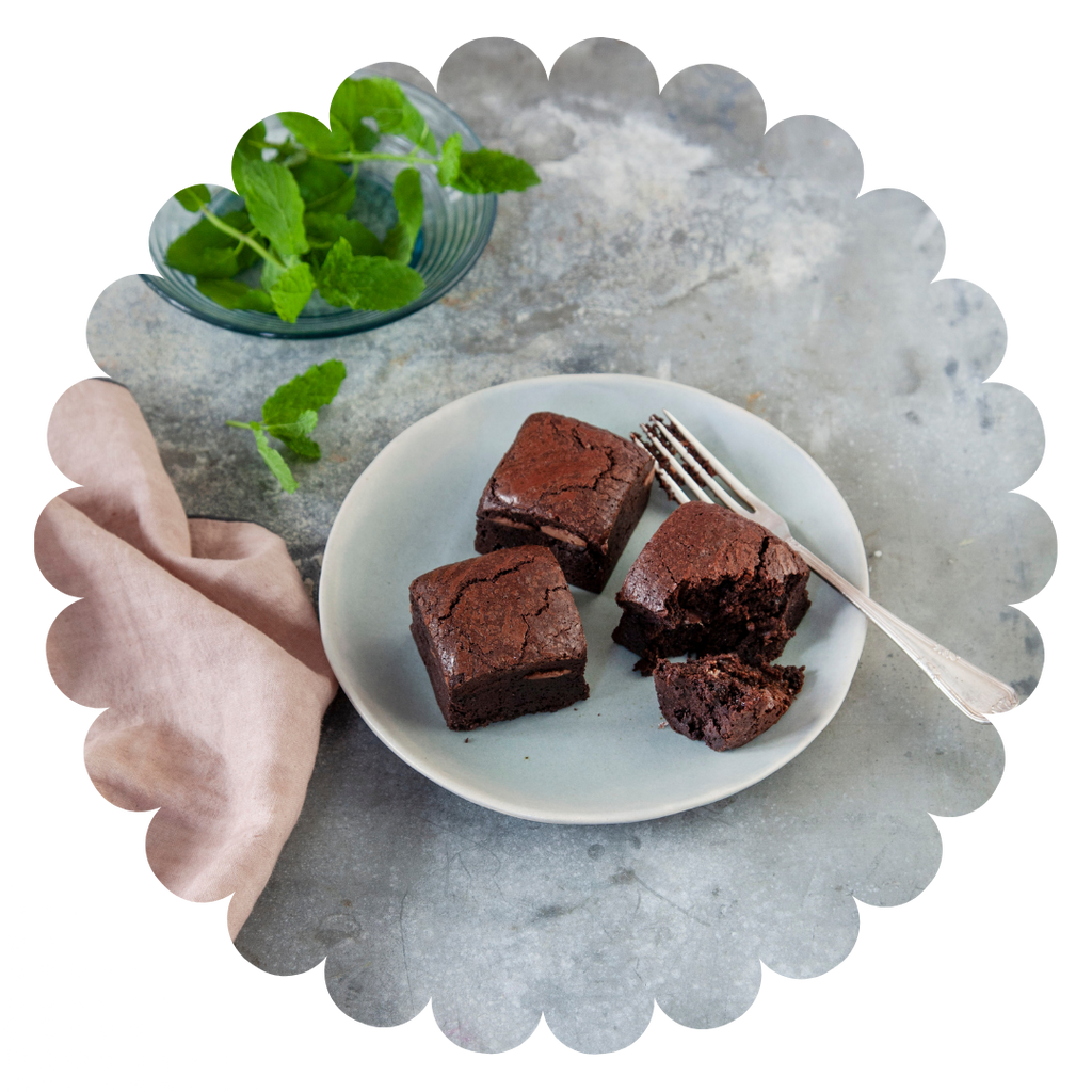 Moist mint flavoured gluten free chocolate brownies on a plate with fresh mint