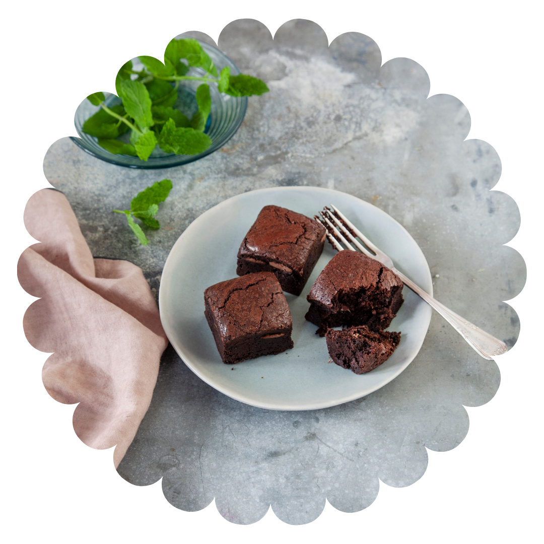 Moist mint flavoured gluten free chocolate brownies on a plate with fresh mint